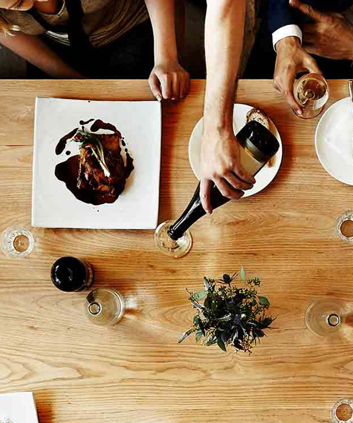Gedeckter Tisch aus der Vogelperspektive, umgeben von Personen, die sich unterhalten und essen.